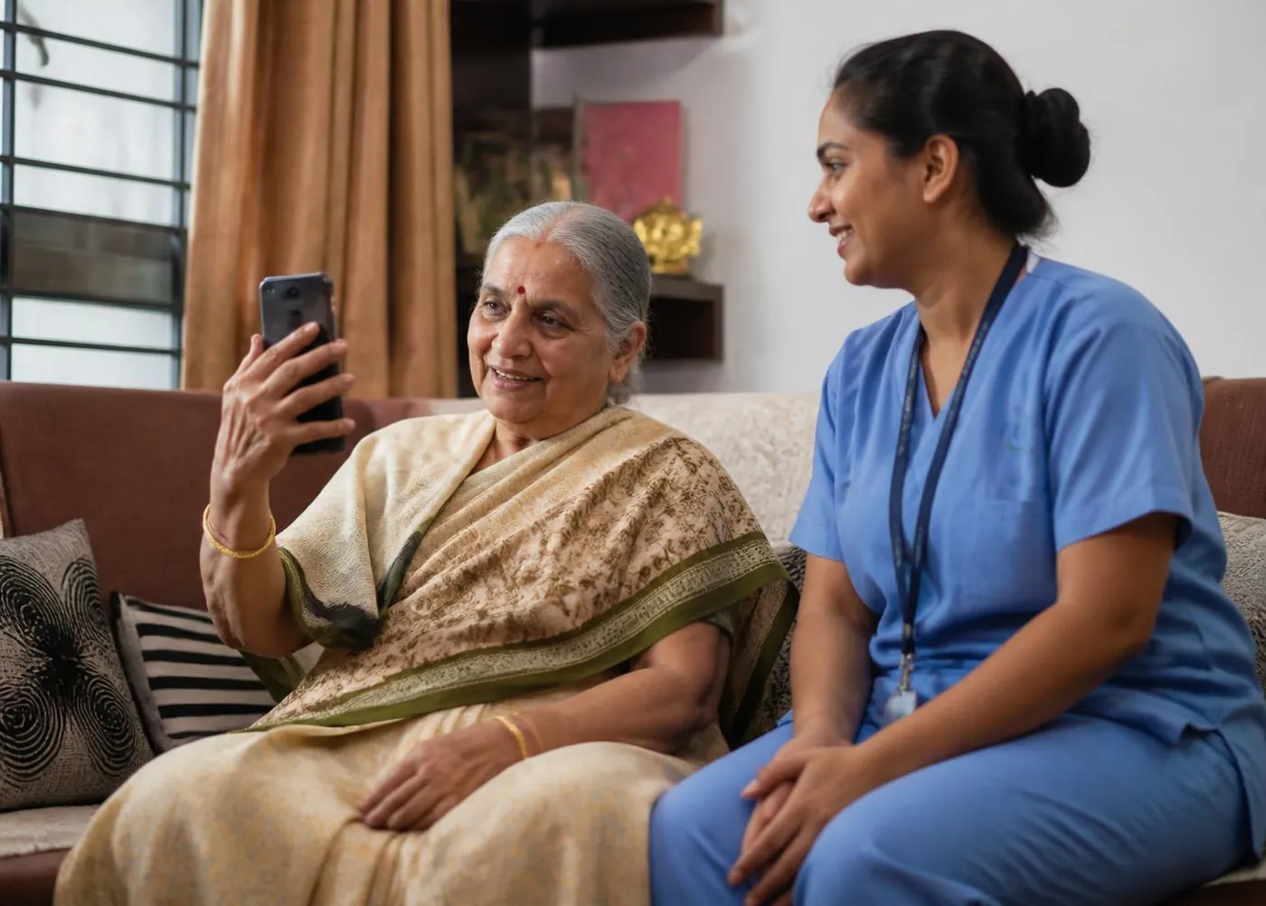 An elderly mother on a video call with her child while a caregiver sits beside her